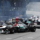Michael Schumacher (C) of Germany and Mercedes GP goes round the first corner while in the background Kamui Kobayashi (R) of Japan and Sauber F1 is launched into the air as he touches wheels with the spinning Romain Grosjean (L) of France and Lotus at the