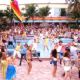A large group of partygoers – including Kelly (Kelly Clarkson, in blue top) and Justin (Justin Guarini, in coral shirt and white T-shirt) – celebrate Spring Break, in song and dance.
